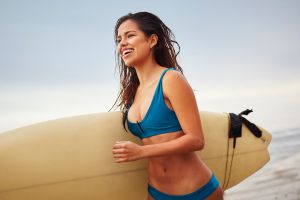 Young woman running on beach carrying surfboard, San Diego, California, USA