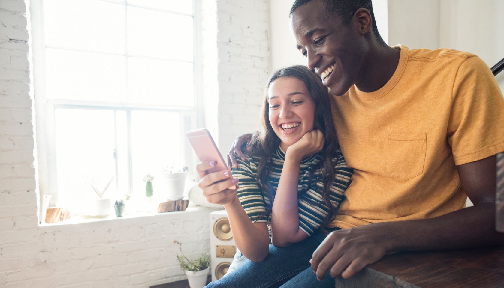 Happy young couple sitting on stairs in a loft sharing cell phone