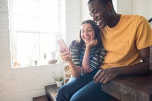 Happy young couple sitting on stairs in a loft sharing cell phone
