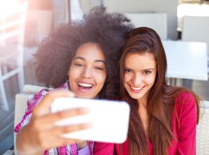 Two smiling female friends driniking coffee and taking selfie