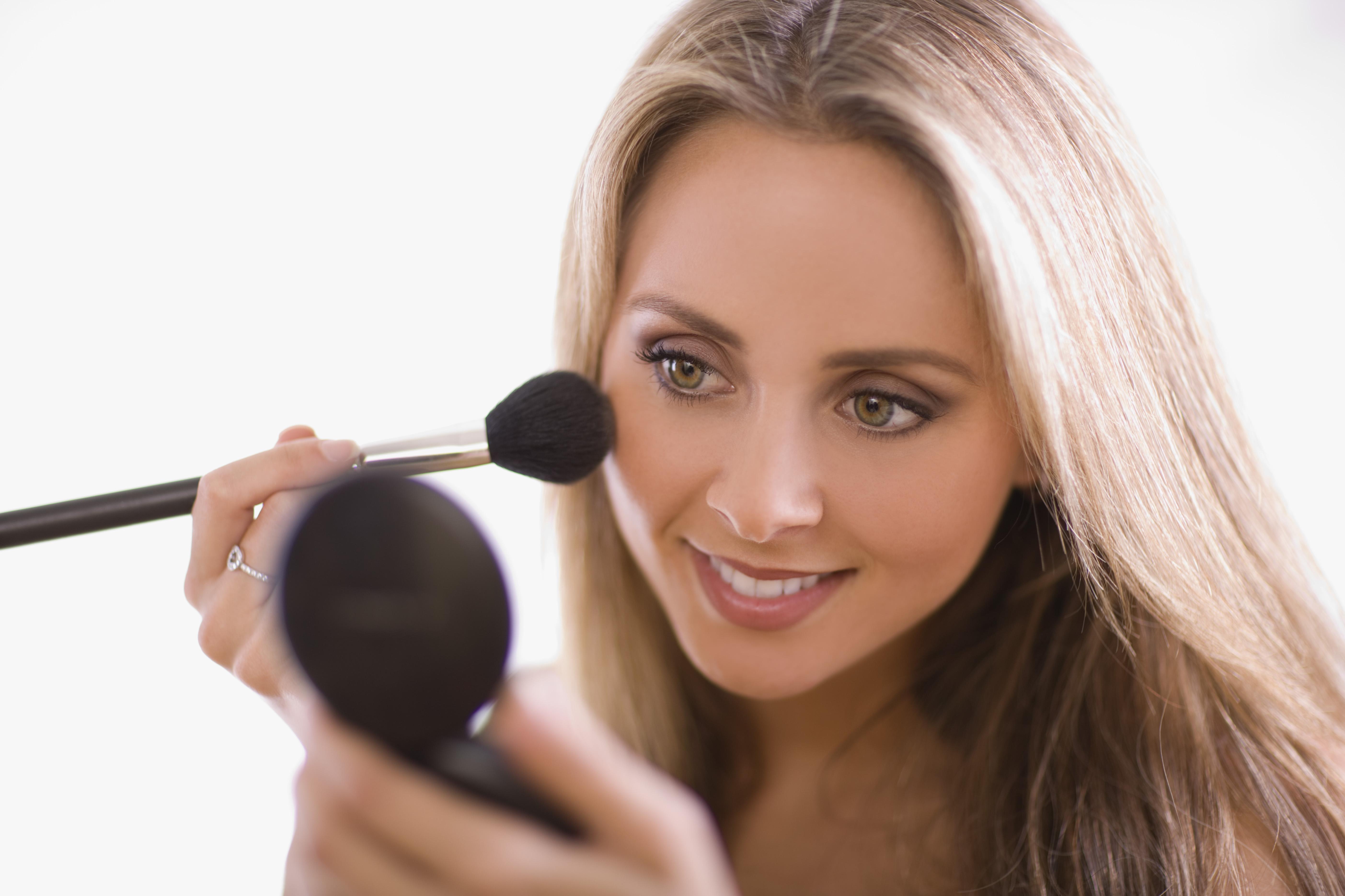 Woman applying blush using compact mirror